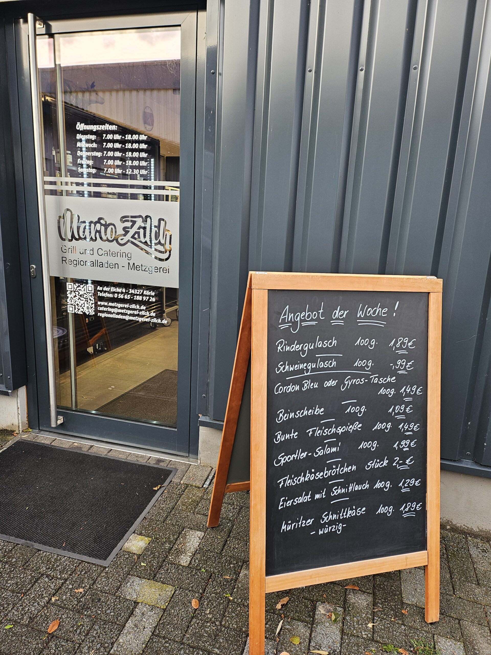 Angebot der Woche an der Tafel vor dem Laden: Rindergulasch 100 g 1,89 €; Schweinegulasch 100 g 0,99 €; Cordon Bleu oder Gyros-Tasche 100 g 1,49 €; Beinscheibe 100 g 1,09 €; Bunte Fleischspieße 100 g 1,49 €; Sportler-Salami 100 g 1,99 €; Fleischkäsebrötchen Stück 2,00 €; Eiersalat mit Schnittlauch 100 g 1,29 €; Müritzer Schnittkäse würzig 100 g 1,89 €
